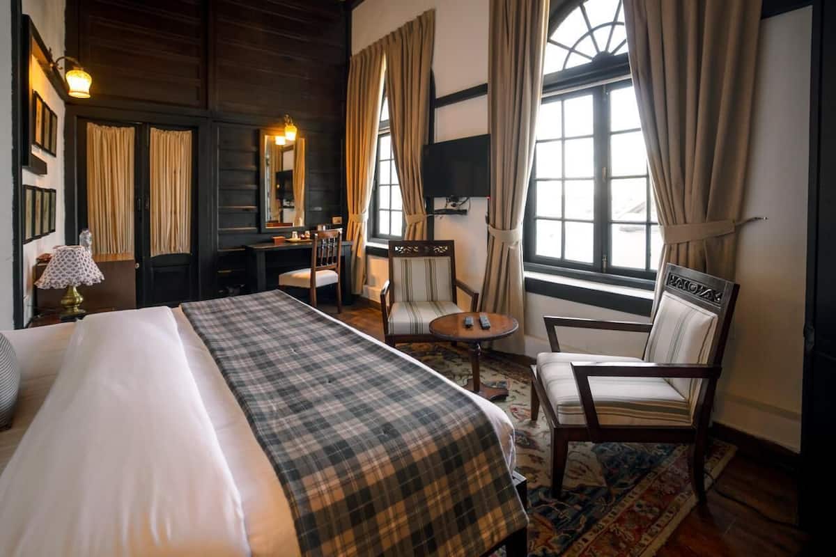 Una habitación de hotel con una cama, una silla, una mesita, un espejo y una ventana con cortinas.