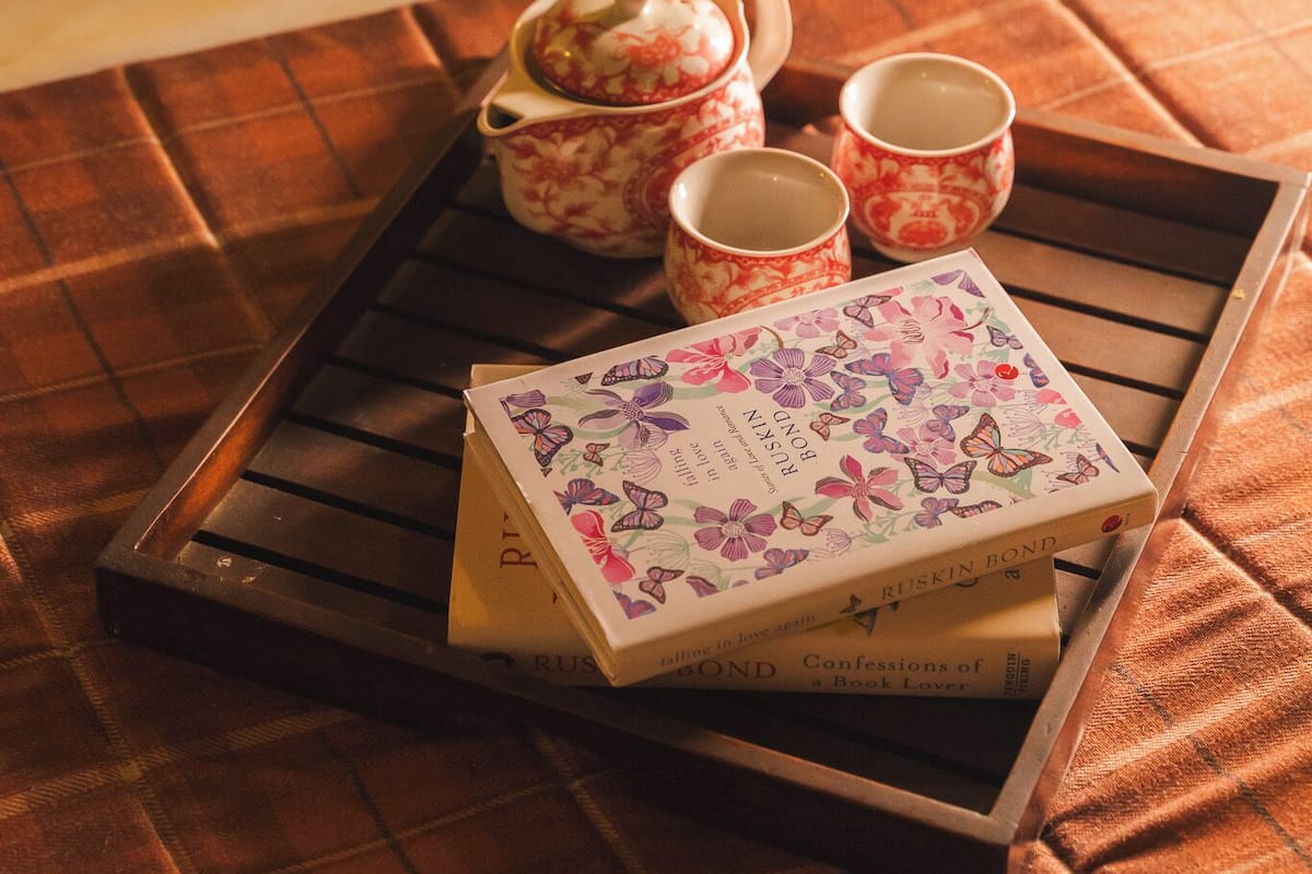 Una bandeja con tetera, tazas y libros sobre un mantel a cuadros.