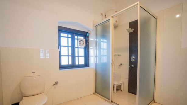 A bathroom with a toilet, a window, and a glass-enclosed shower area. - Ilbert Manor (Dehradun)