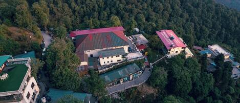 An aerial view of a building complex surrounded by dense forest, featuring multiple structures with red roofs and a green lawn area.