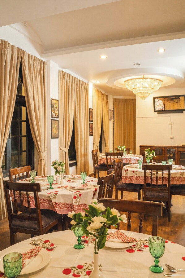 A dining area with multiple tables set for meals, featuring floral tablecloths and green glassware.