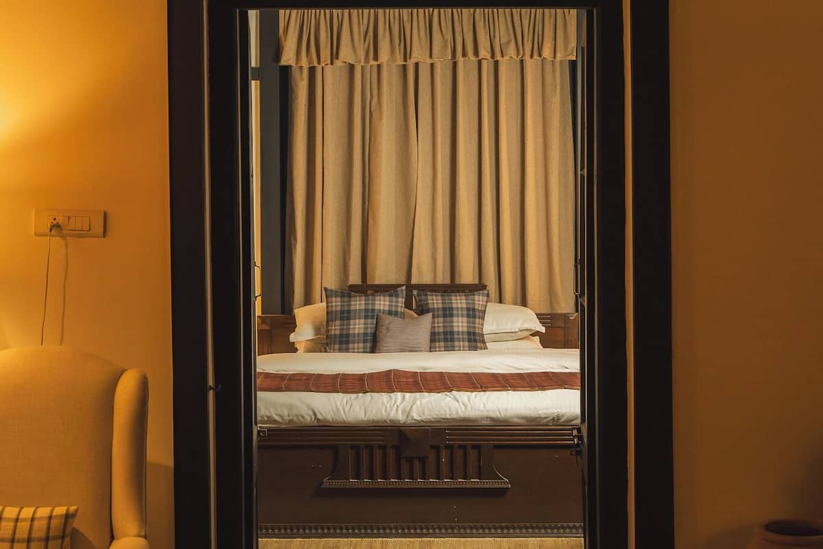 Un dormitorio con cama, cortinas, una silla y suelo de madera.