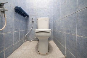 A bathroom with a toilet, a hand dryer, and a visible pipe. - OYO 94102 Kuningan Guest House Syariah (Bandung)