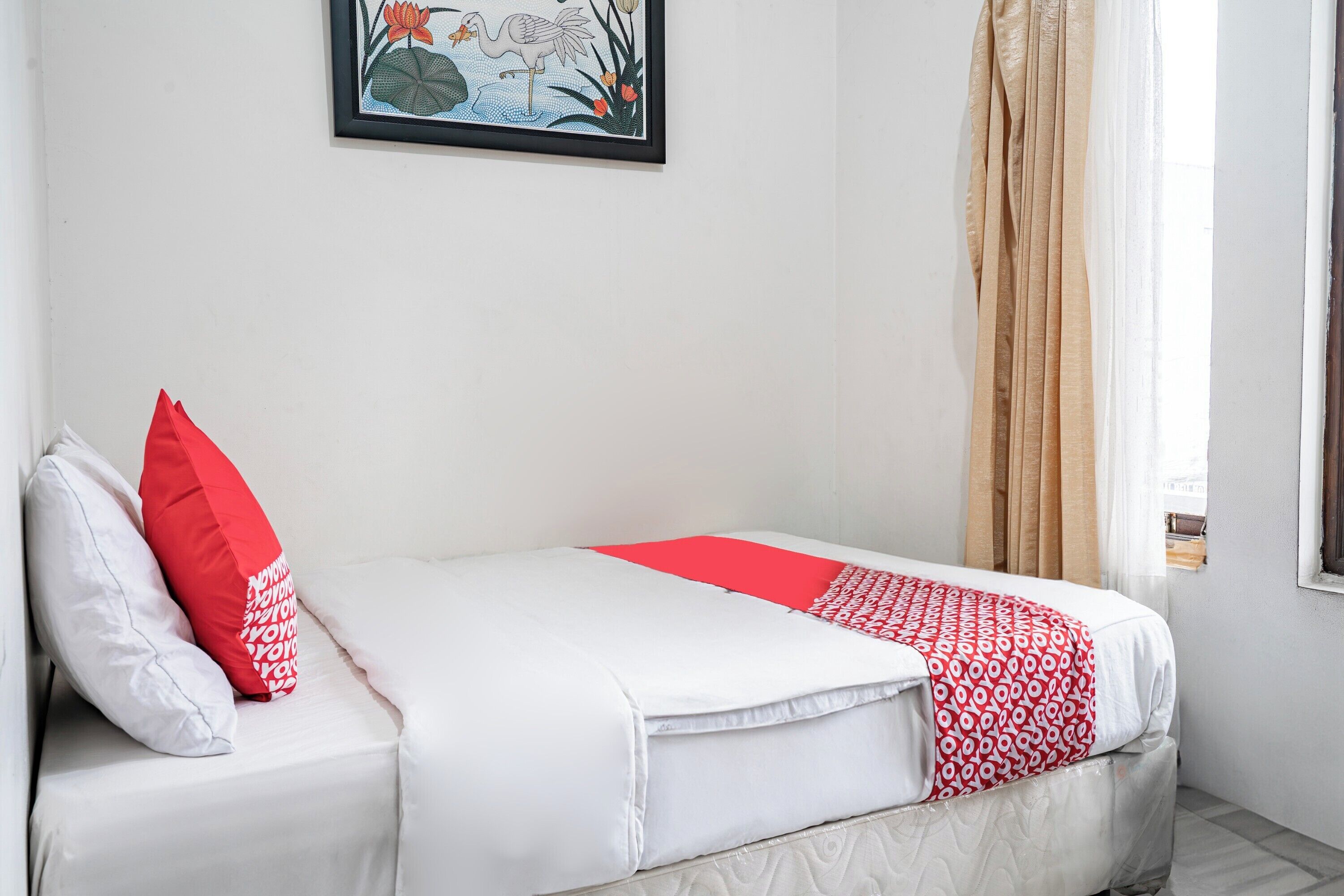 A neatly made bed with white and red bedding, a framed picture on the wall, and a window with curtains.