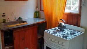 Una cocina con armarios de madera, estufa a gas, ventana con cortinas naranjas y un lavamanos.