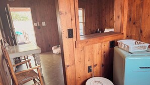 Ein kleiner Raum mit Holzwänden, einem Tisch mit Stühlen, einem Kühlschrank und einer Mülltonne.