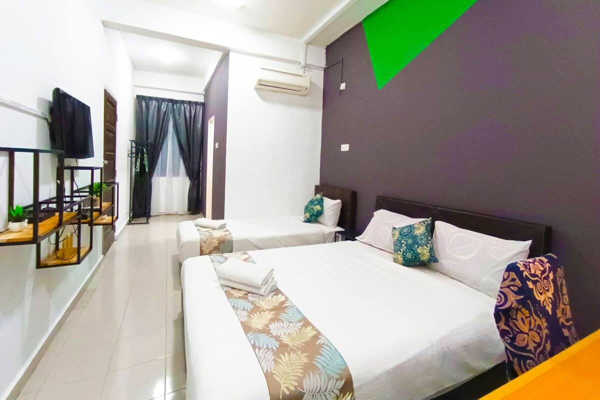 Une chambre d’hôtel avec deux lits, une télévision, un bureau et une fenêtre avec des rideaux.