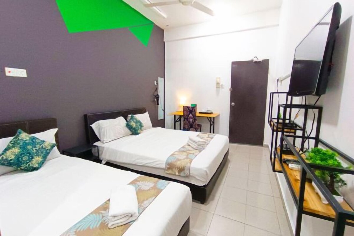 A hotel room with two beds, a flat-screen TV mounted on the wall, a small table with a lamp, and a door.