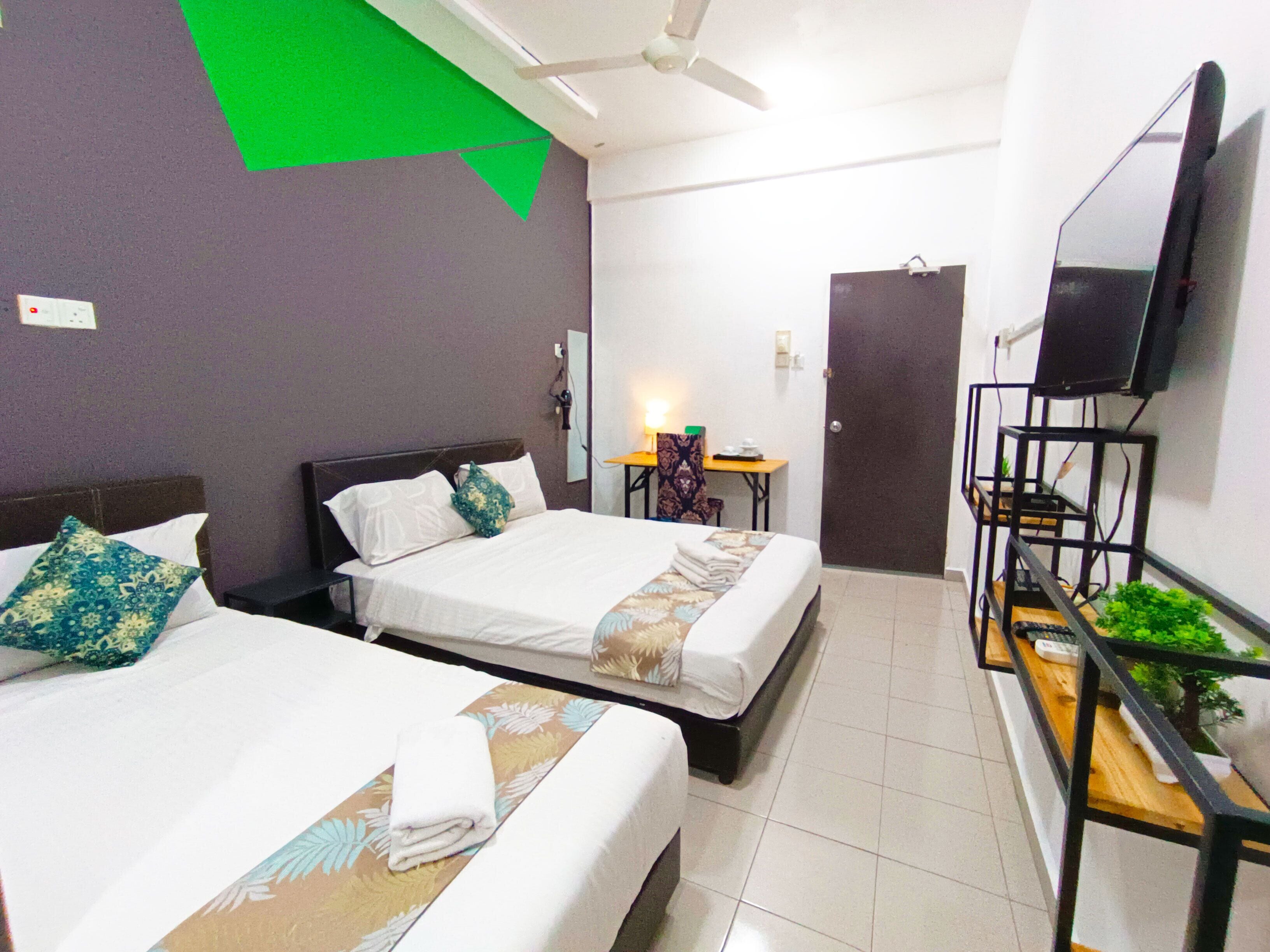 Habitación de hotel con dos camas, un escritorio, una silla, un televisor y una planta.