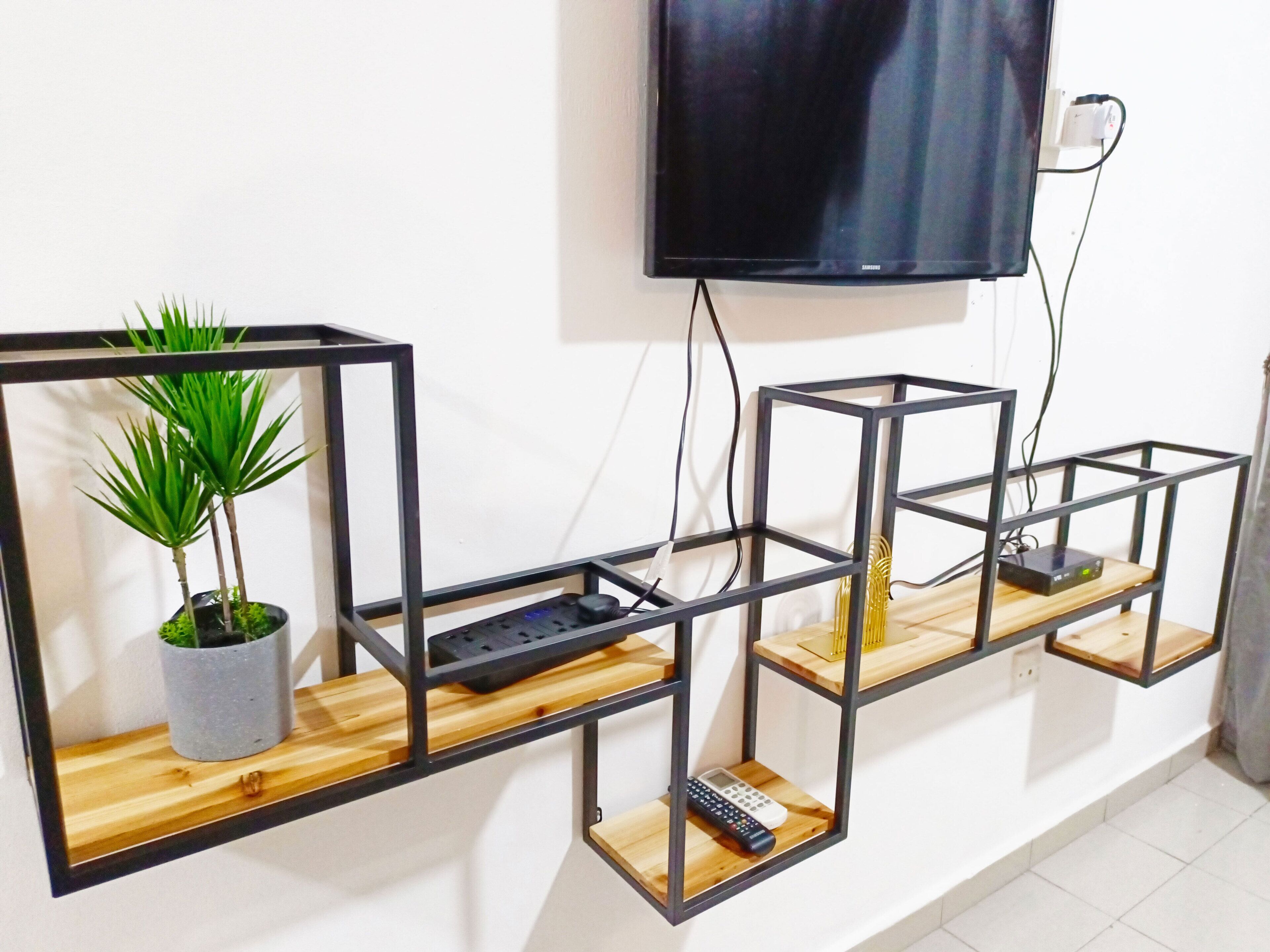 Un interior moderno con un televisor de pantalla plana montado en la pared, rodeado de estanterías de metal negro con repisas de madera.