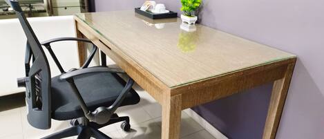 A wooden desk with a glass top, a black office chair, a small potted plant, and a white object on the desk.