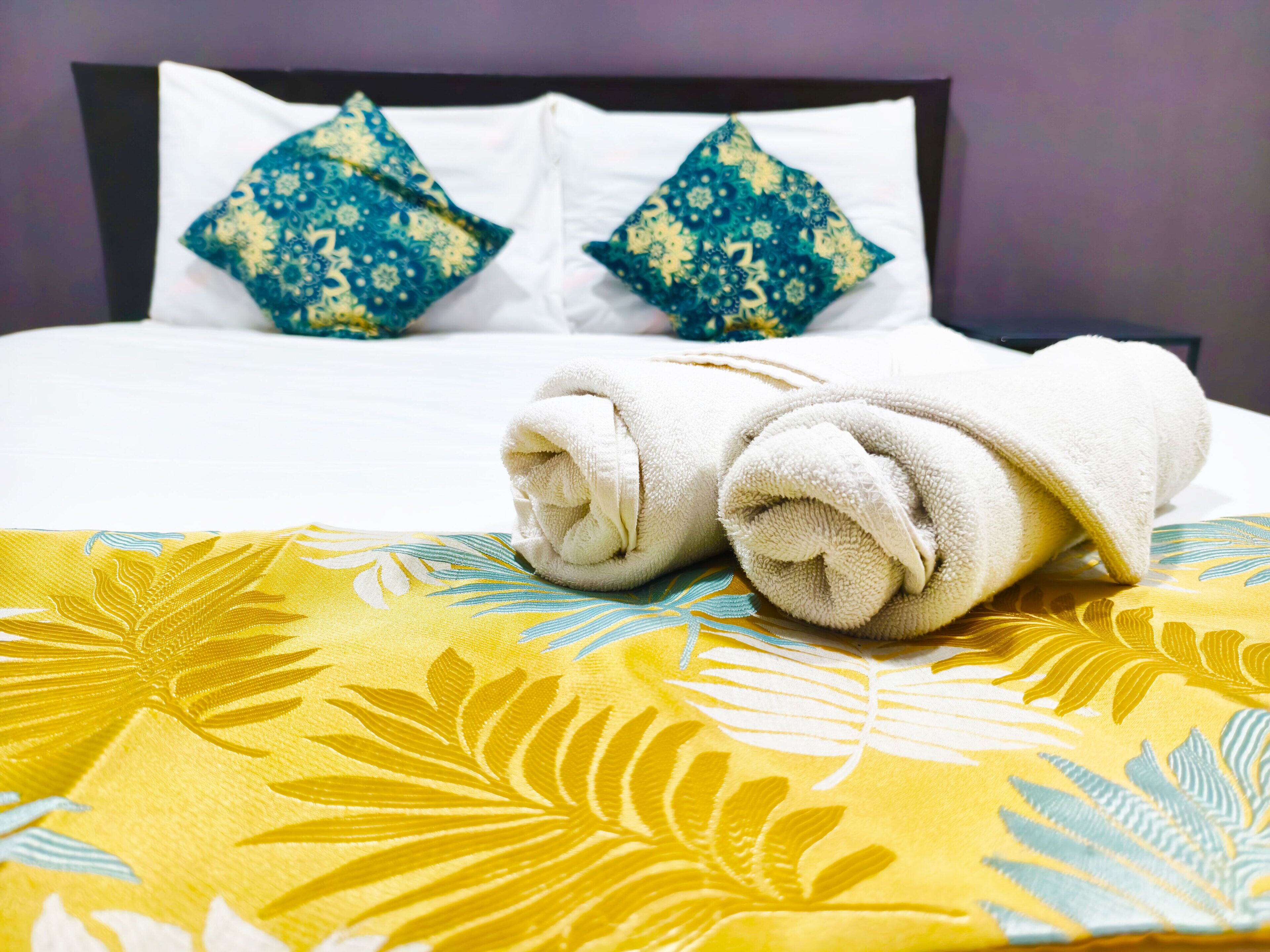 Un lit bien fait, recouvert d’une couvre-lit à motifs floraux et agrémenté de deux coussins décoratifs.