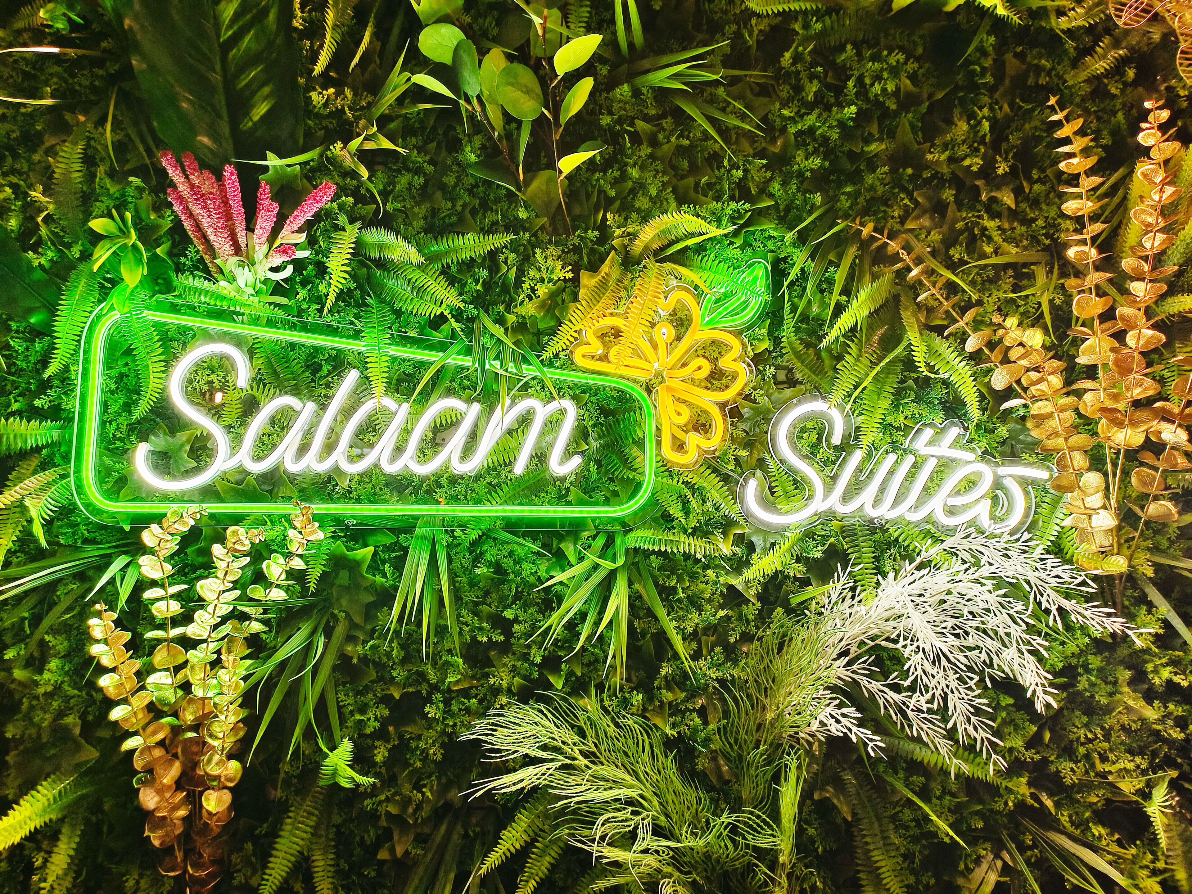 Un letrero de neón que dice 'Salaam Suites' en medio de abundante follaje.