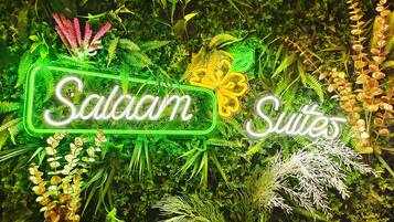 Ein Neon-Schild für 'Salaam Suites' inmitten üppiger Vegetation.