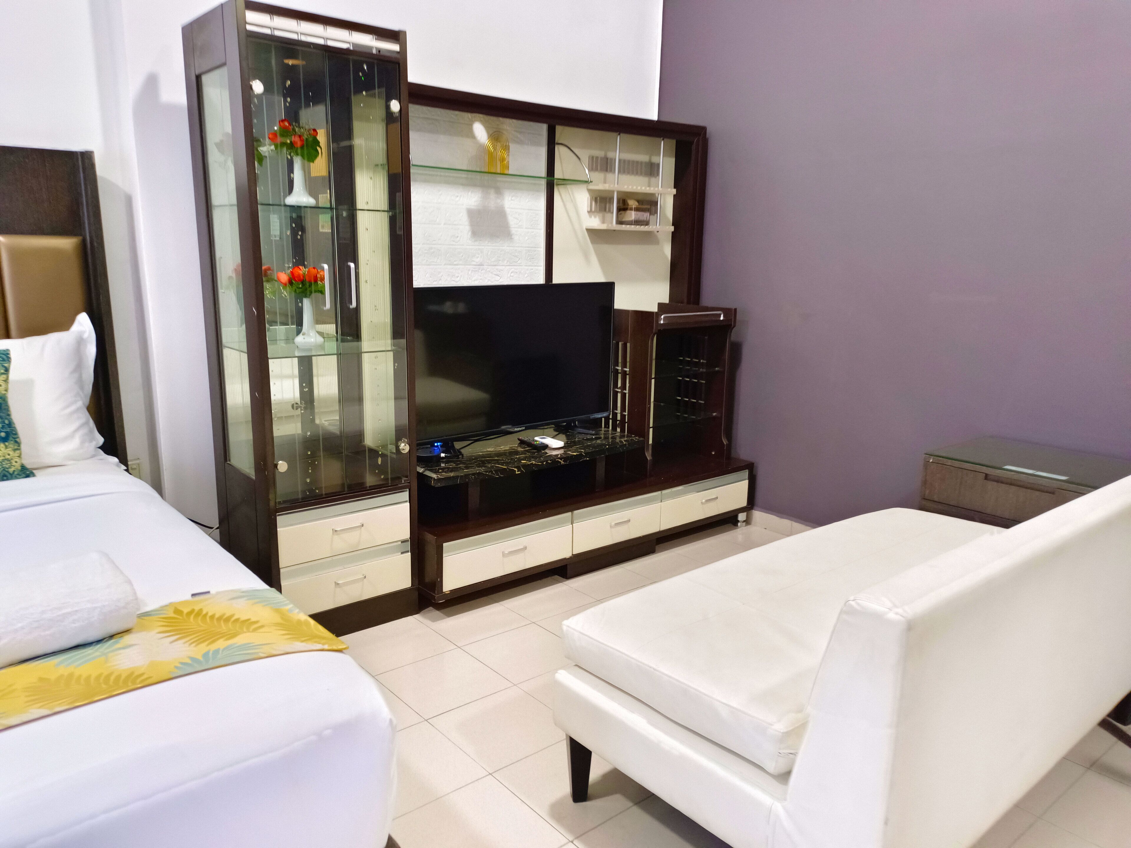 Une chambre d’hôtel comprenant un lit, un canapé, une télévision et une vitrine contenant des objets décoratifs.