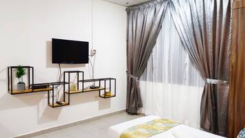 Una habitación de hotel con cama, televisor montado en la pared y ventana con cortinas.