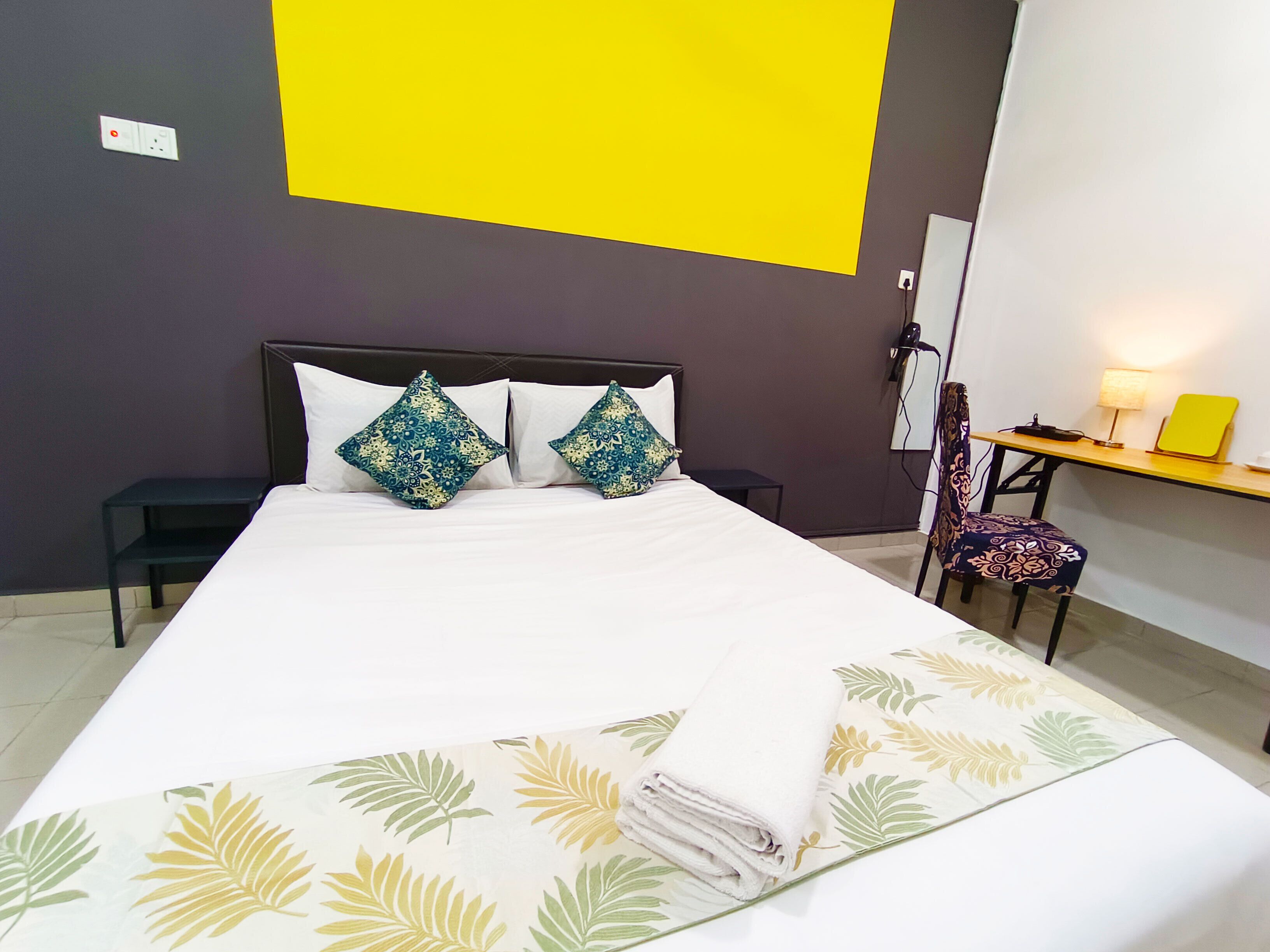 A hotel room with a bed, a desk, a chair, and a lamp.