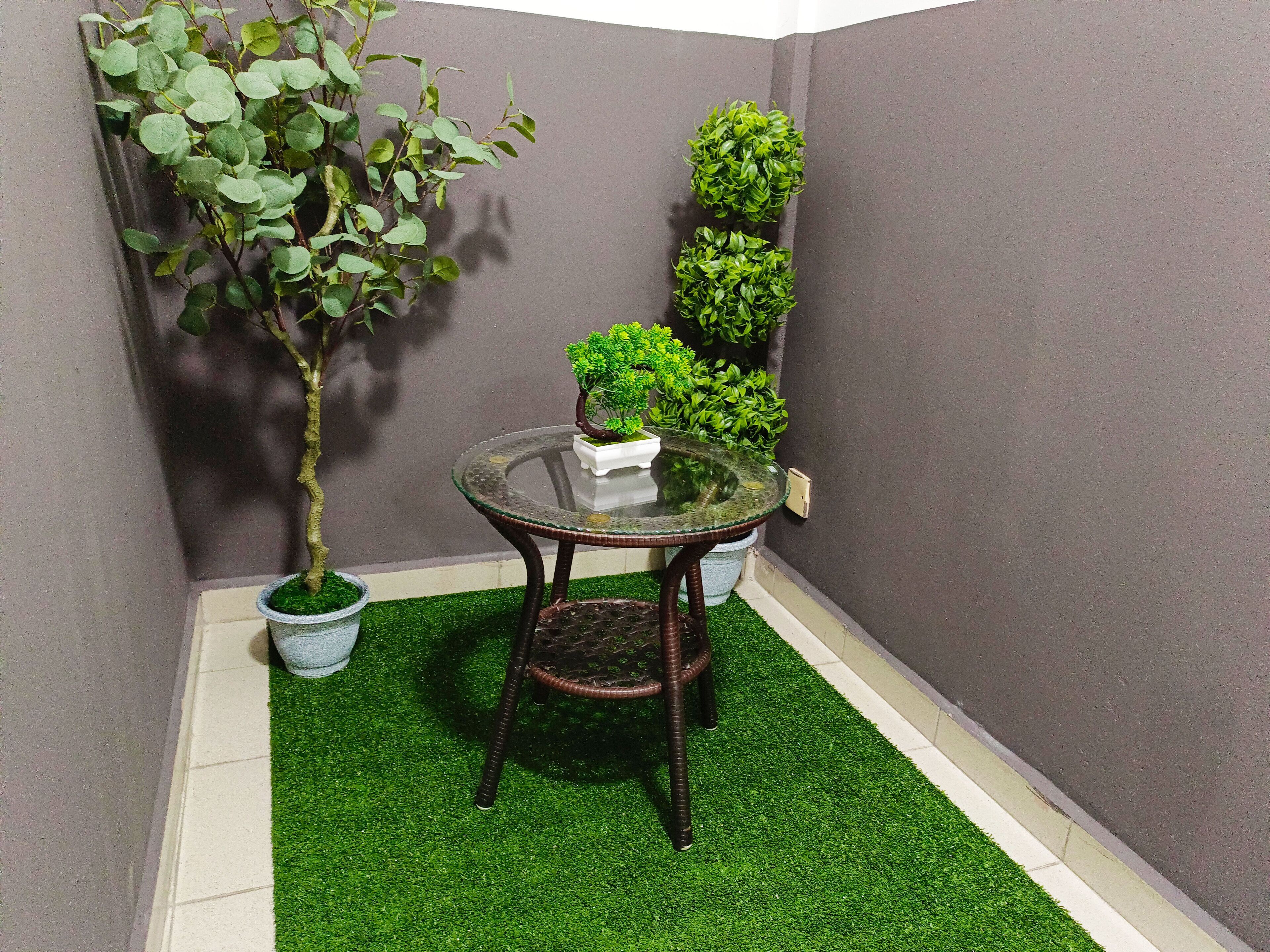 A small, enclosed outdoor area with artificial green turf, a glass table with a metal frame, and potted plants.