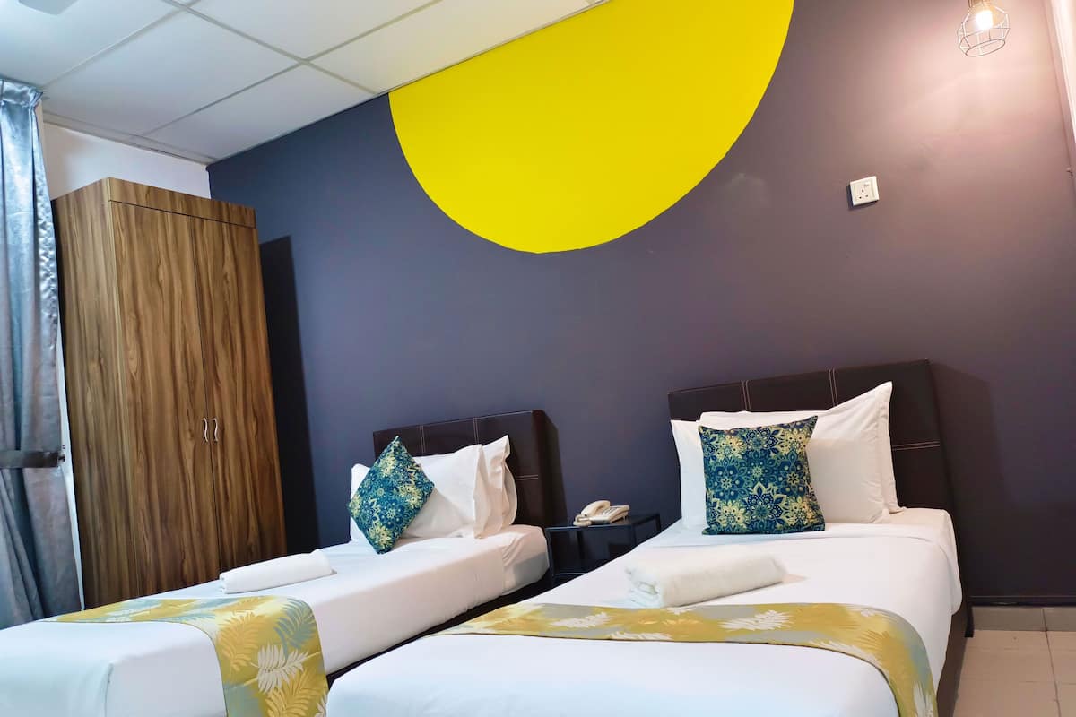 Une chambre d’hôtel avec deux lits, une armoire en bois, un grand élément de décoration murale jaune et un luminaire suspendu.