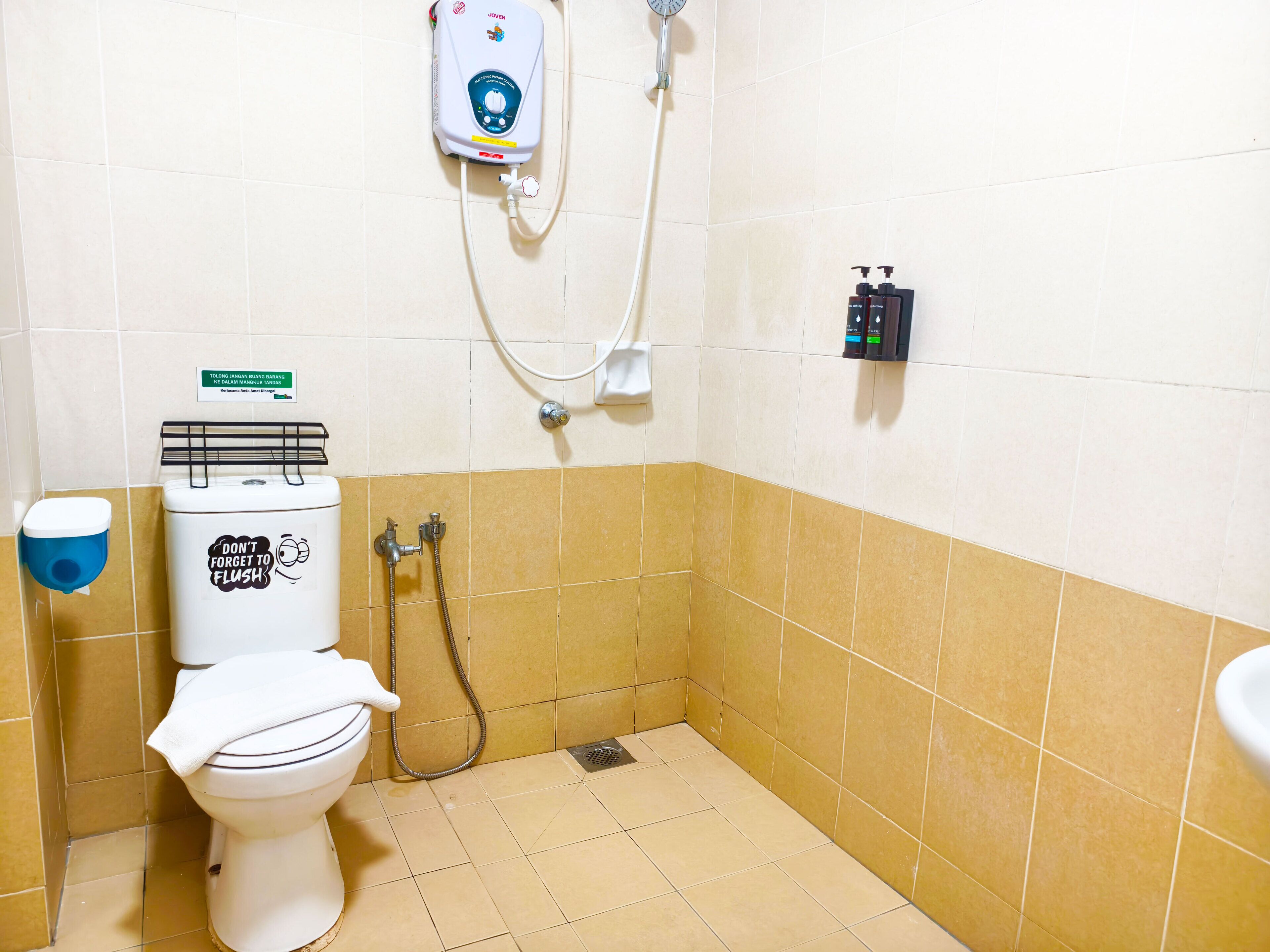 Un baño pequeño con inodoro, secamanos, ducha y dispensador de jabón en la pared.