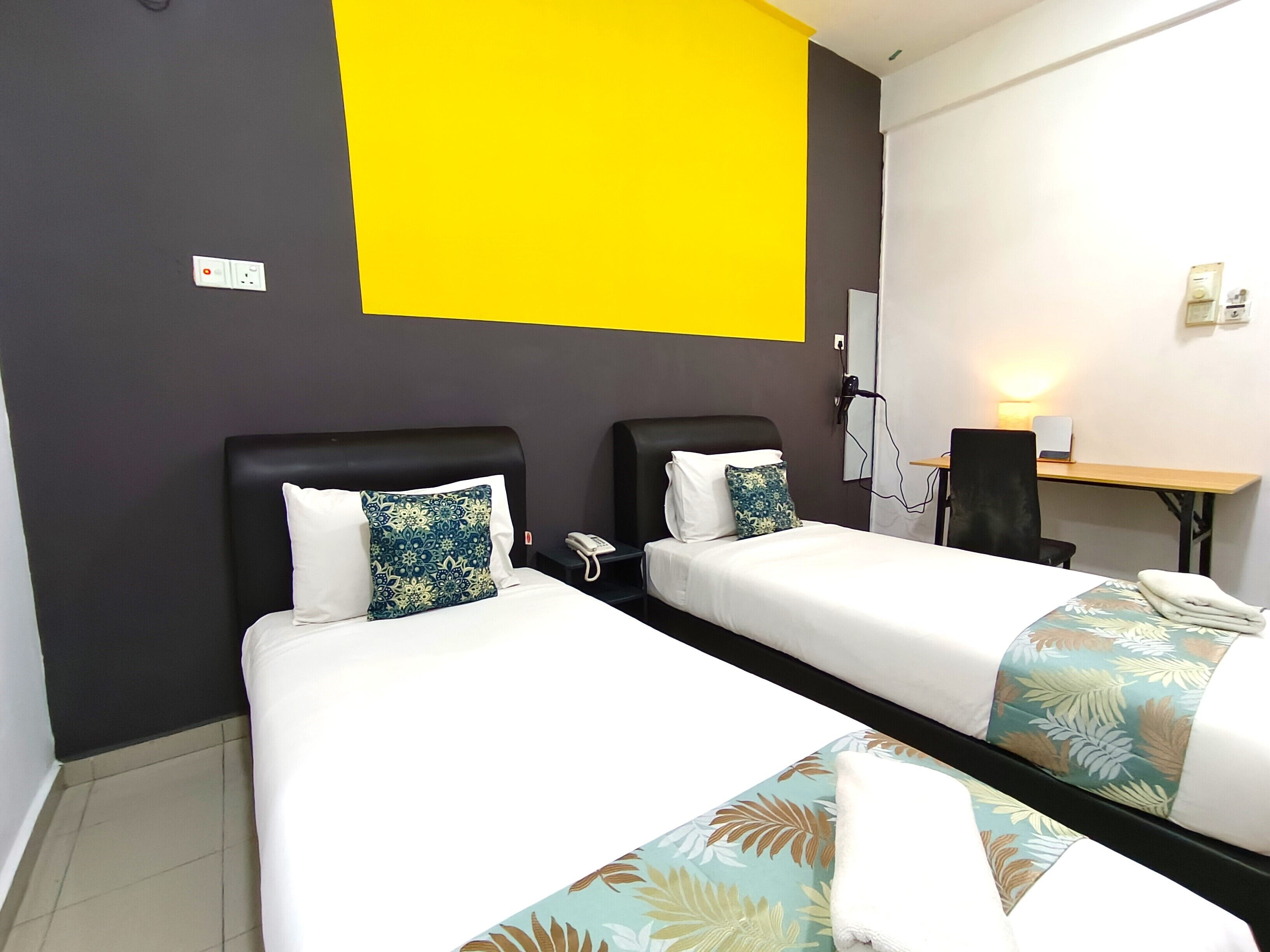 A hotel room with two single beds, a desk, and a chair.
