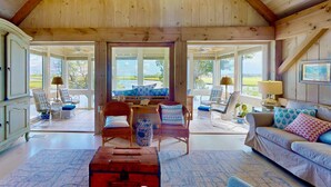 A spacious living room with wooden beams, a large window, and a view of the outdoors. - Seaglass - Waterfront, Incredible Views of BHI Creek, 3 Suites, Pool, Kayaks, BHI Club+Golf, Dogs OK (Bald Head Island)