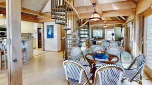 A spacious dining area with a round table and wicker chairs, a spiral staircase, and wooden beams on the ceiling. - Seaglass - Waterfront, Incredible Views of BHI Creek, 3 Suites, Pool, Kayaks, BHI Club+Golf, Dogs OK (Bald Head Island)