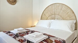 Ein Bett mit einem gewobenen Kopfteil, weißen Bettwäsche und einer gemusterten Tagesdecke.