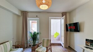 Ein Wohnzimmer mit einer Couch, Sesseln, einem Fernseher und einer Topfpflanze.