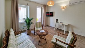 Ein Wohnzimmer mit einer Couch, Sesseln, einem Tisch, einem Fernseher und einer Zimmerpflanze.