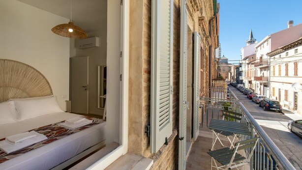 Ein Hotelzimmer mit Bett, einer Hängelampe, einem Balkon mit Stühlen und Blick auf die Straße.