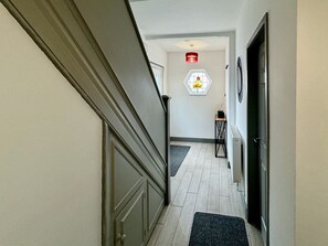 A hallway with a wooden door, a small table with a chair, a hexagonal window, and a red light fixture. - Lenhurst House – Contractors, Families, Holidays (Cleethorpes)