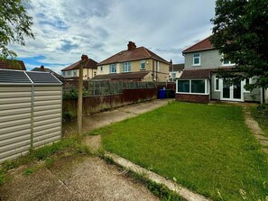 A residential backyard with a grassy lawn, a wooden fence, and houses in the background. - Lenhurst House – Contractors, Families, Holidays (Cleethorpes)