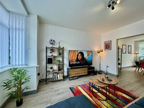 Una sala de estar moderna con un televisor de pantalla plana, una estantería, una mesa de centro y una alfombra colorida.