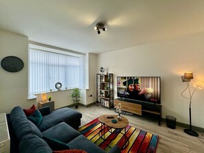 Una sala de estar con sofá, televisor, estantería y ventana con persianas.