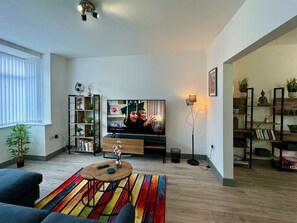 A living room with a TV, bookshelf, and a colorful rug. - Lenhurst House – Contractors, Families, Holidays (Cleethorpes)