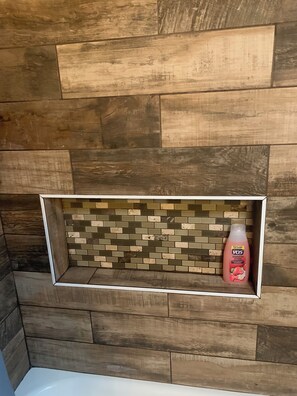 A bathroom with a wooden wall and a shelf containing a bottle of VOS strawberry & cream body wash. - Grimley Gaslight (Las Vegas)
