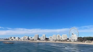 Un paysage urbain côtier avec une grande roue bien visible et des immeubles modernes qui s’élèvent le long de la plage.