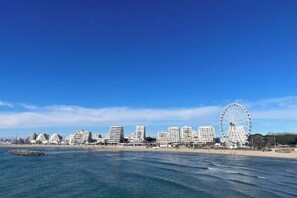 Un paisaje urbano costero con una noria destacada y modernos edificios altos a lo largo de la playa.