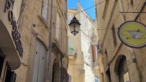 Eine enge Straße mit Gebäuden an beiden Seiten, ein hängender Laternenmast und ein Schild mit einem Logo.