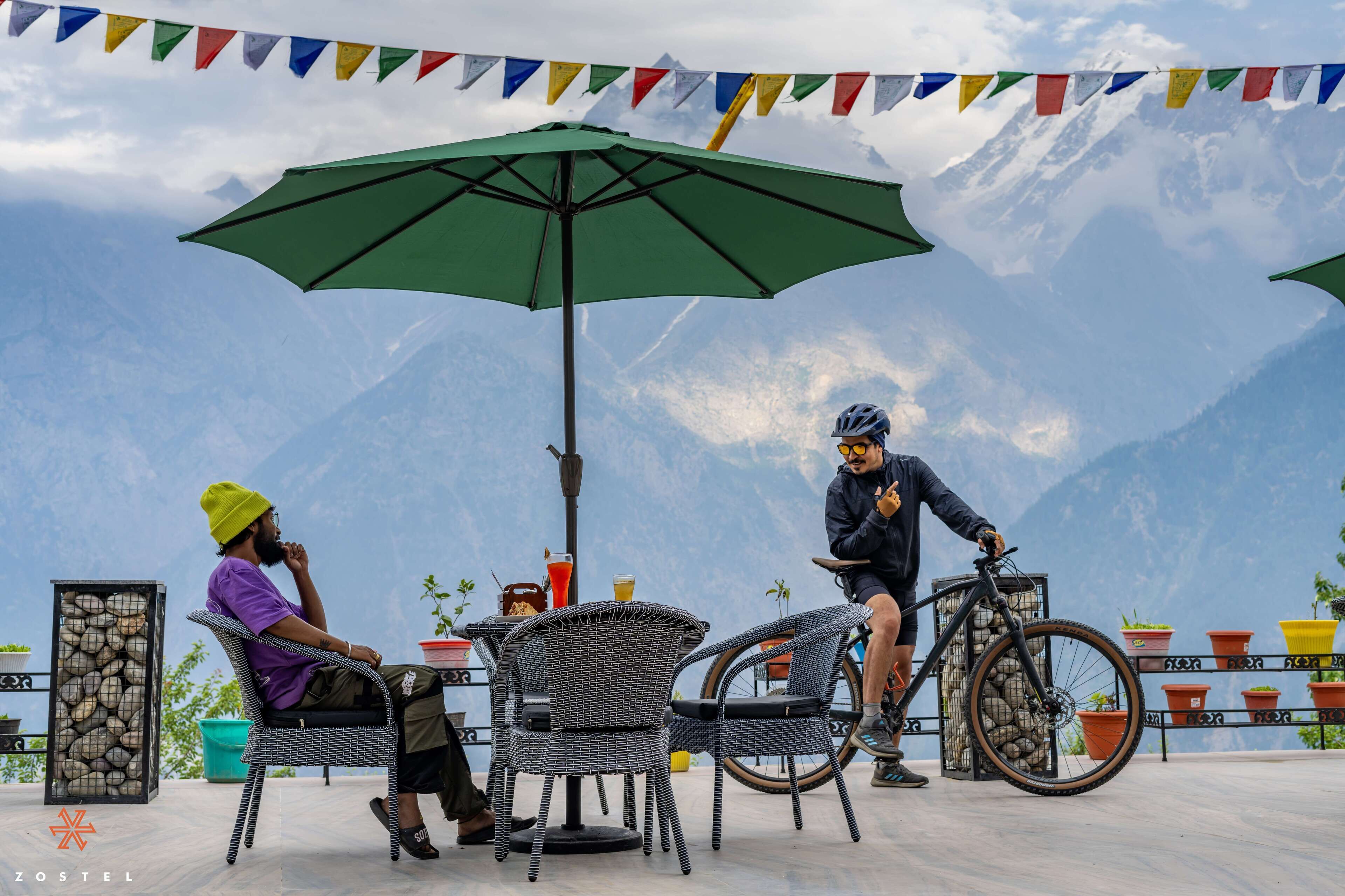 A terrace with wicker chairs, a green umbrella, and a mountain view.