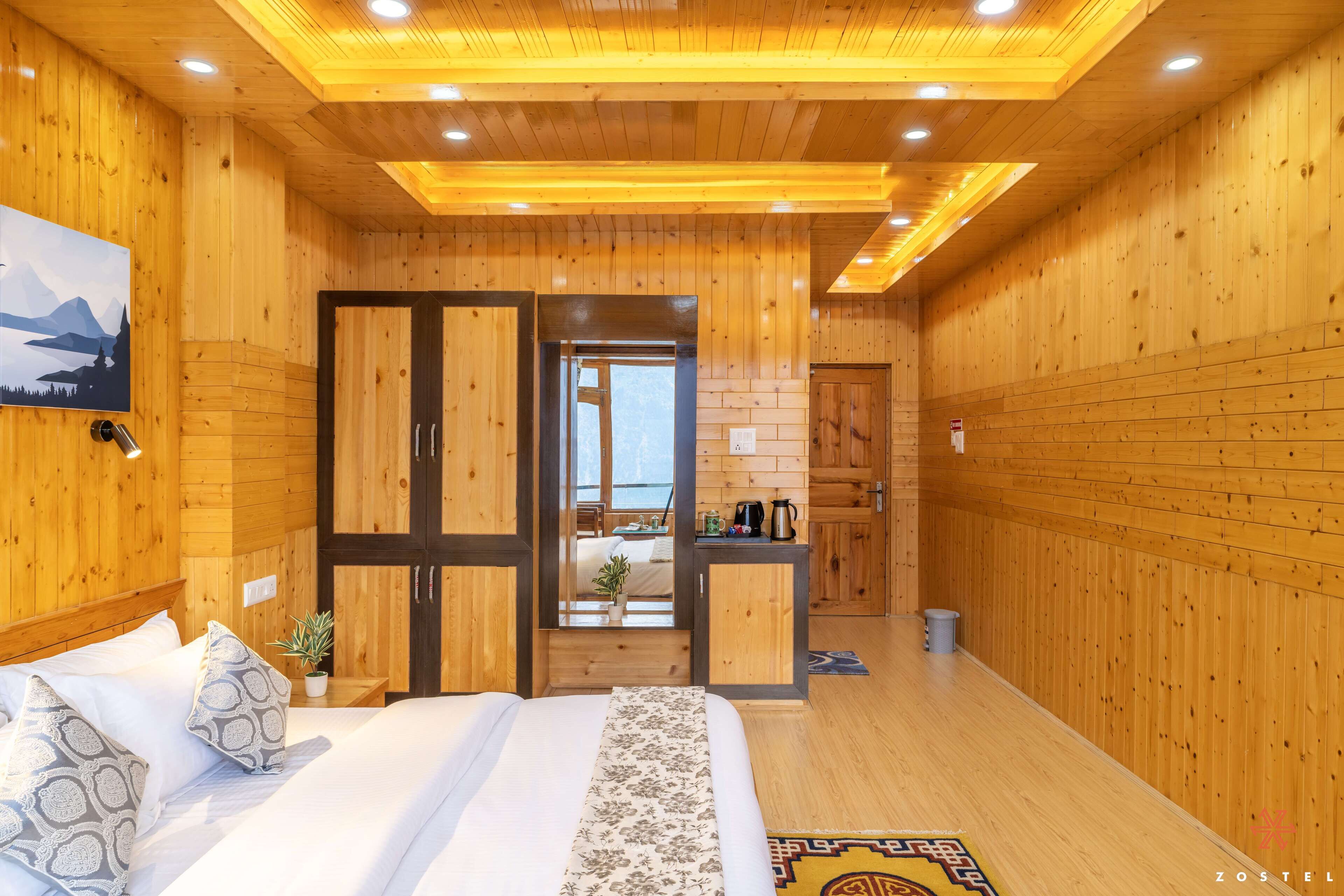 A wooden cabin room with a bed, a desk, and a view of the outdoors.