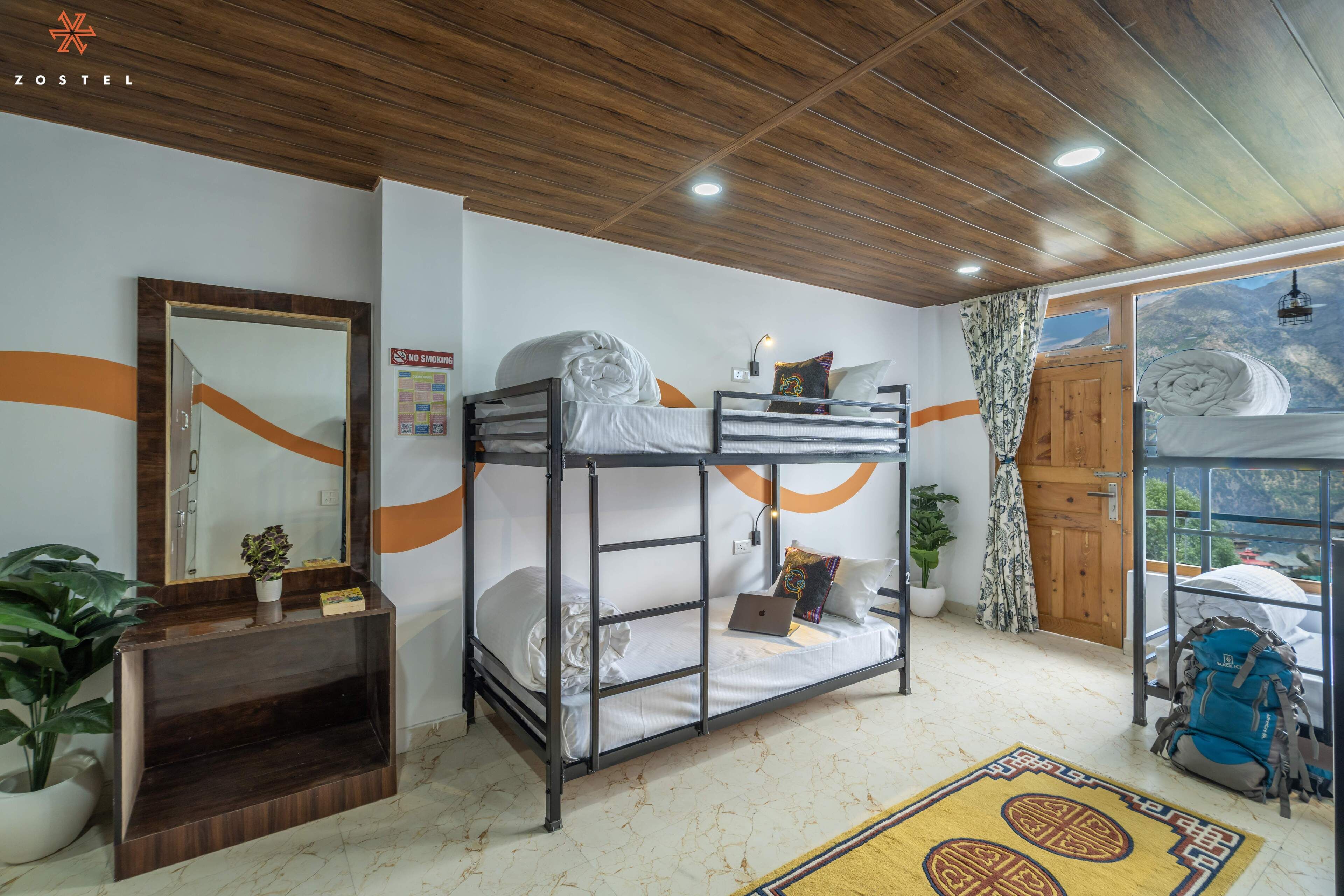 A bunk bed room with a wooden ceiling, a mirror, a desk, and a window with a view.