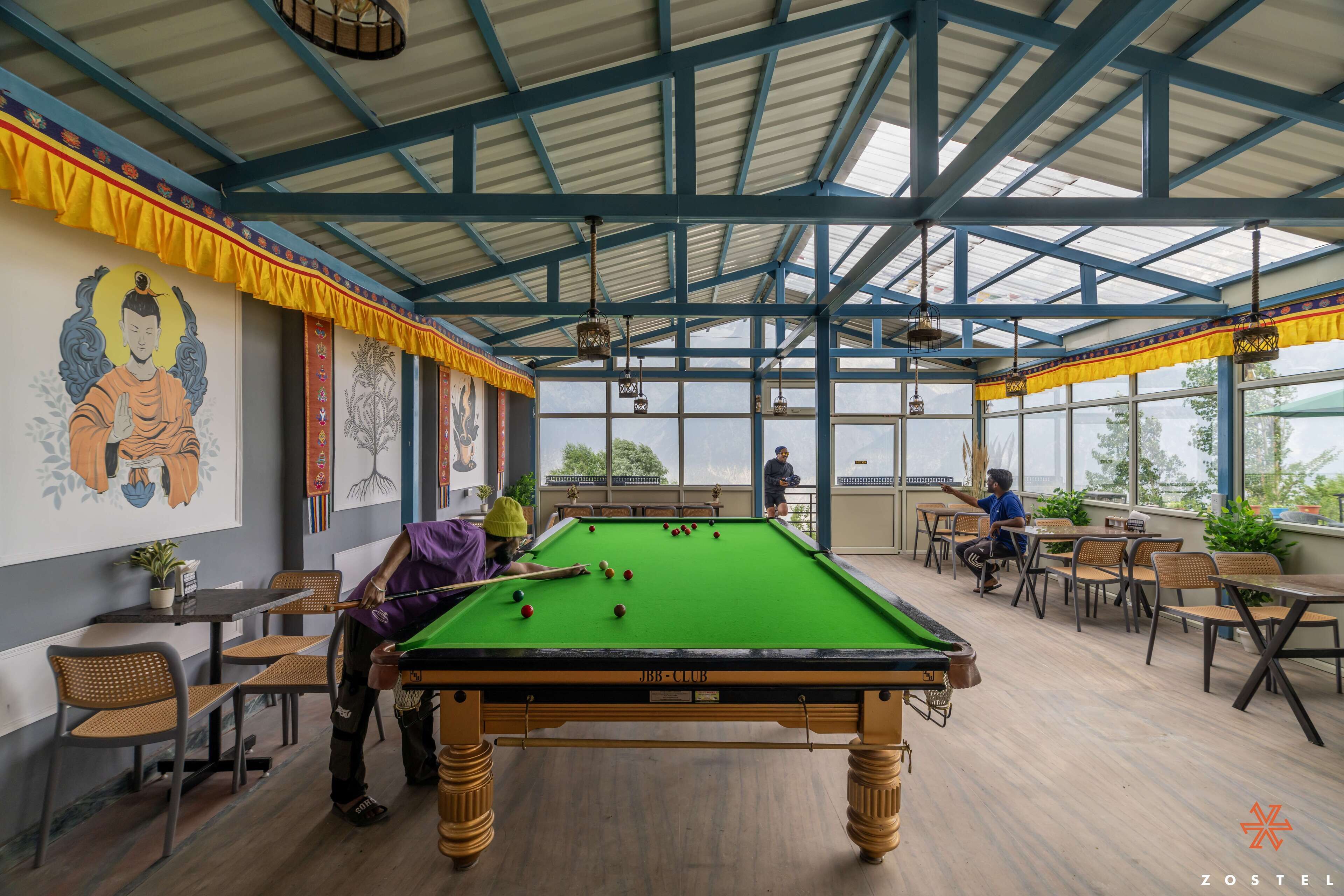 A pool table in a room with a high ceiling and large windows, surrounded by chairs and tables.