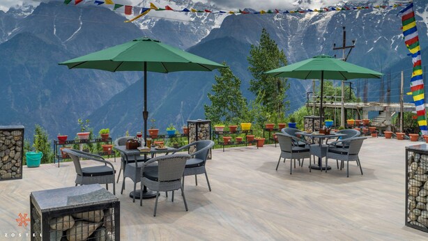 An outdoor seating area with tables and chairs, surrounded by potted plants and a mountainous backdrop. - Zostel Kalpa (Kalpa)