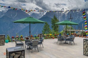 An outdoor seating area with tables and chairs, surrounded by potted plants and a mountainous backdrop. - Zostel Kalpa (Kalpa)