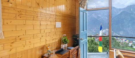 A wooden room with a desk, a chair, a laptop, a plant, and a window with a mountain view.
