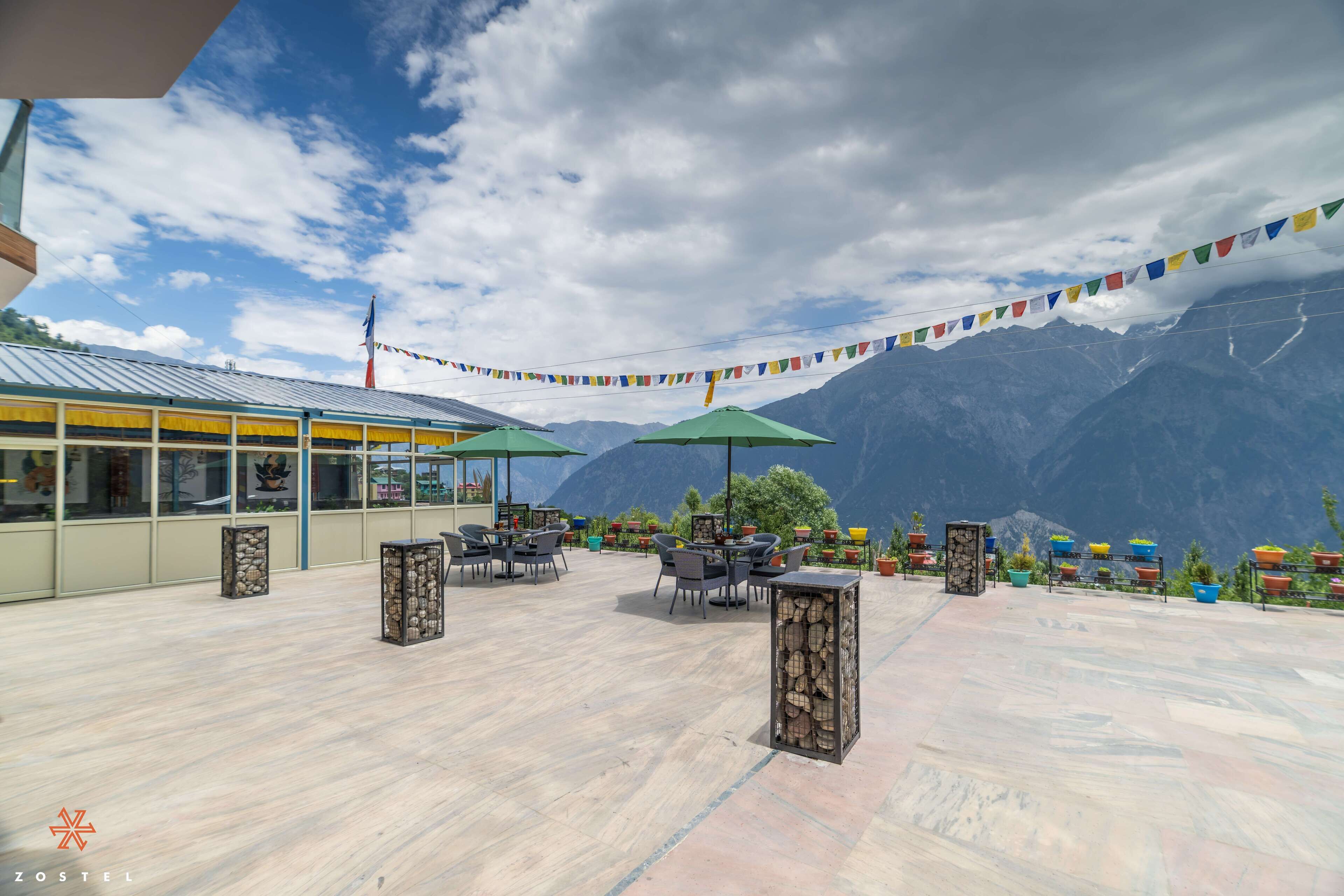 An outdoor seating area with tables and chairs, a stone pillar, and colorful prayer flags.