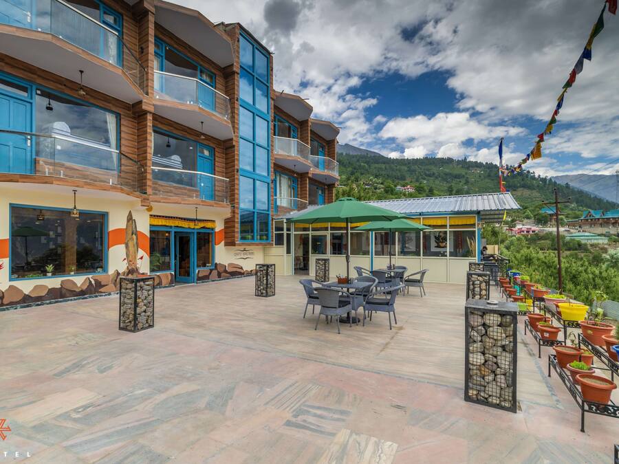 A hotel with a terrace featuring outdoor seating, a mountain view, and traditional decor.