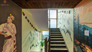 A staircase with a mural on the walls depicting mountains and trees, leading to a window with a view. - Zostel Kalpa (Kalpa)